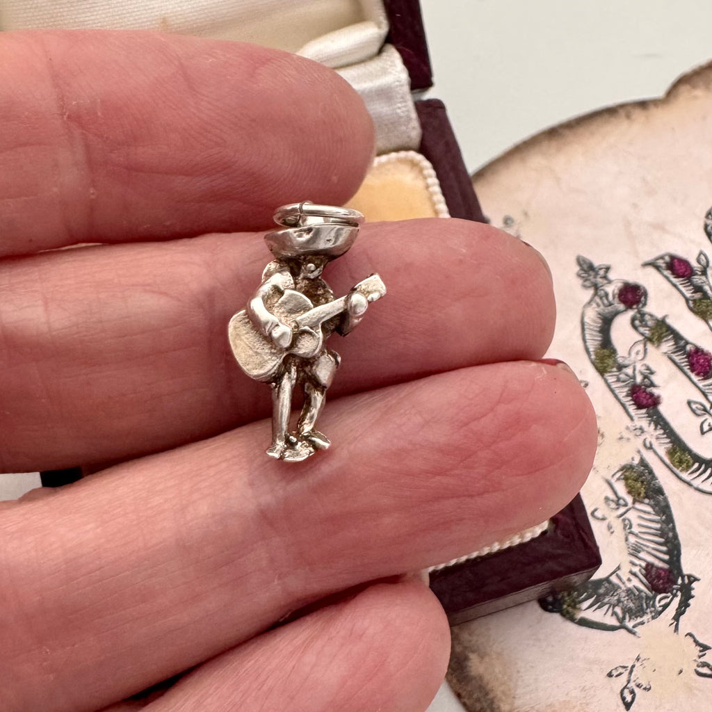 Vintage silver Mexican guitar player charm in a womans hand with a decorative background