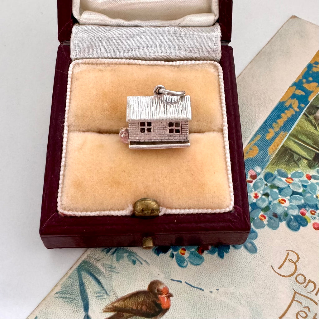 Silver house charm in a jewelry box on a decorative surface with a bird figurine.