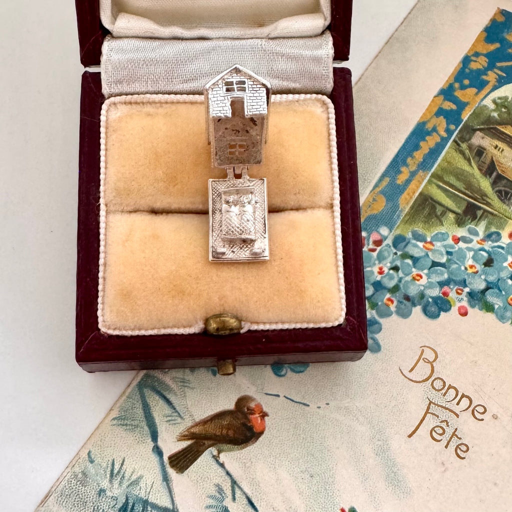 Vintage silver opening house charm in a jewelry box with a decorative card in the background