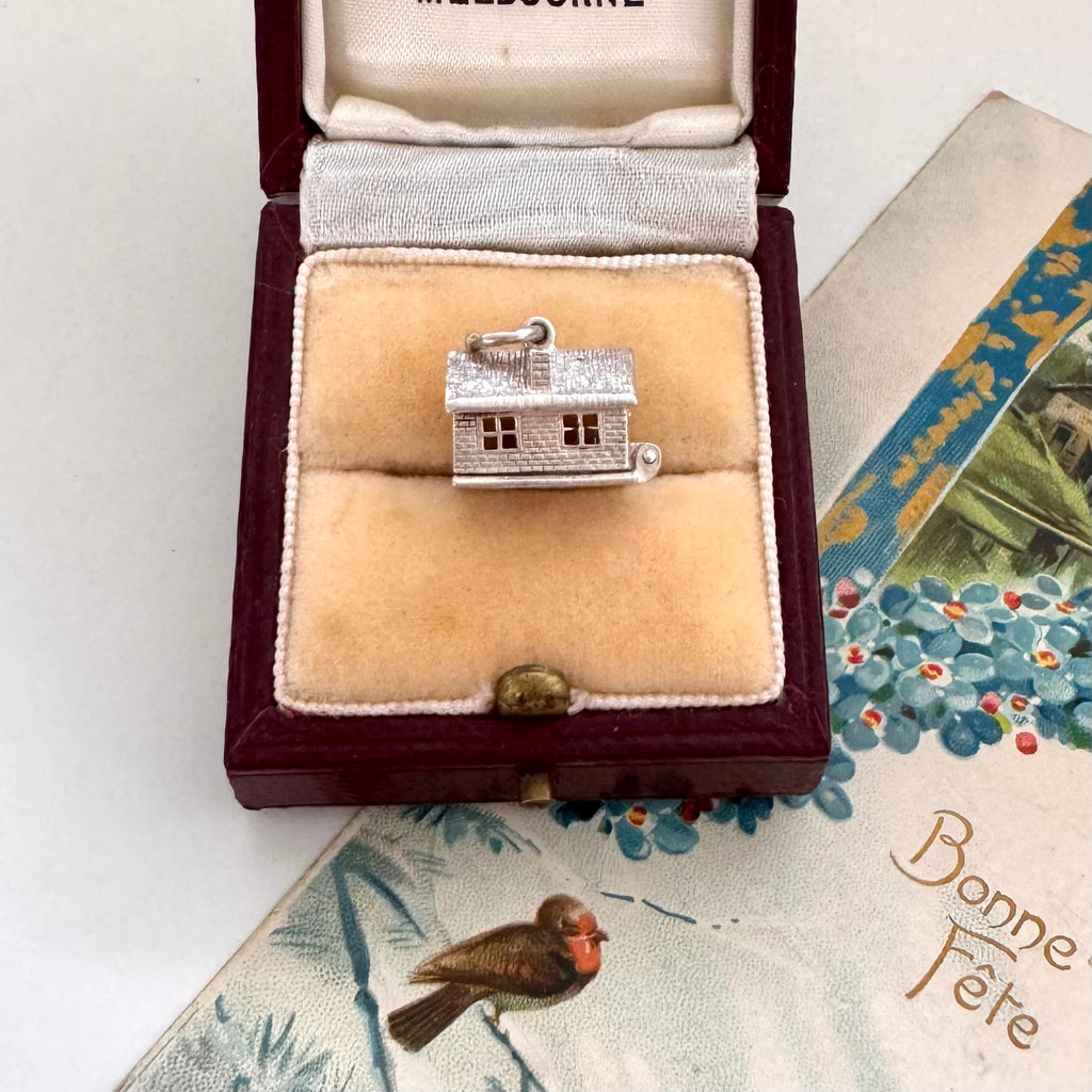Silver house-shaped charm in a jewelry box on a decorative card with floral designs.