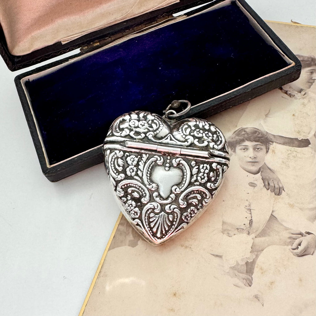 Decorative heart-shaped silver pendant with intricate designs on an open jewelry box and vintage photo.