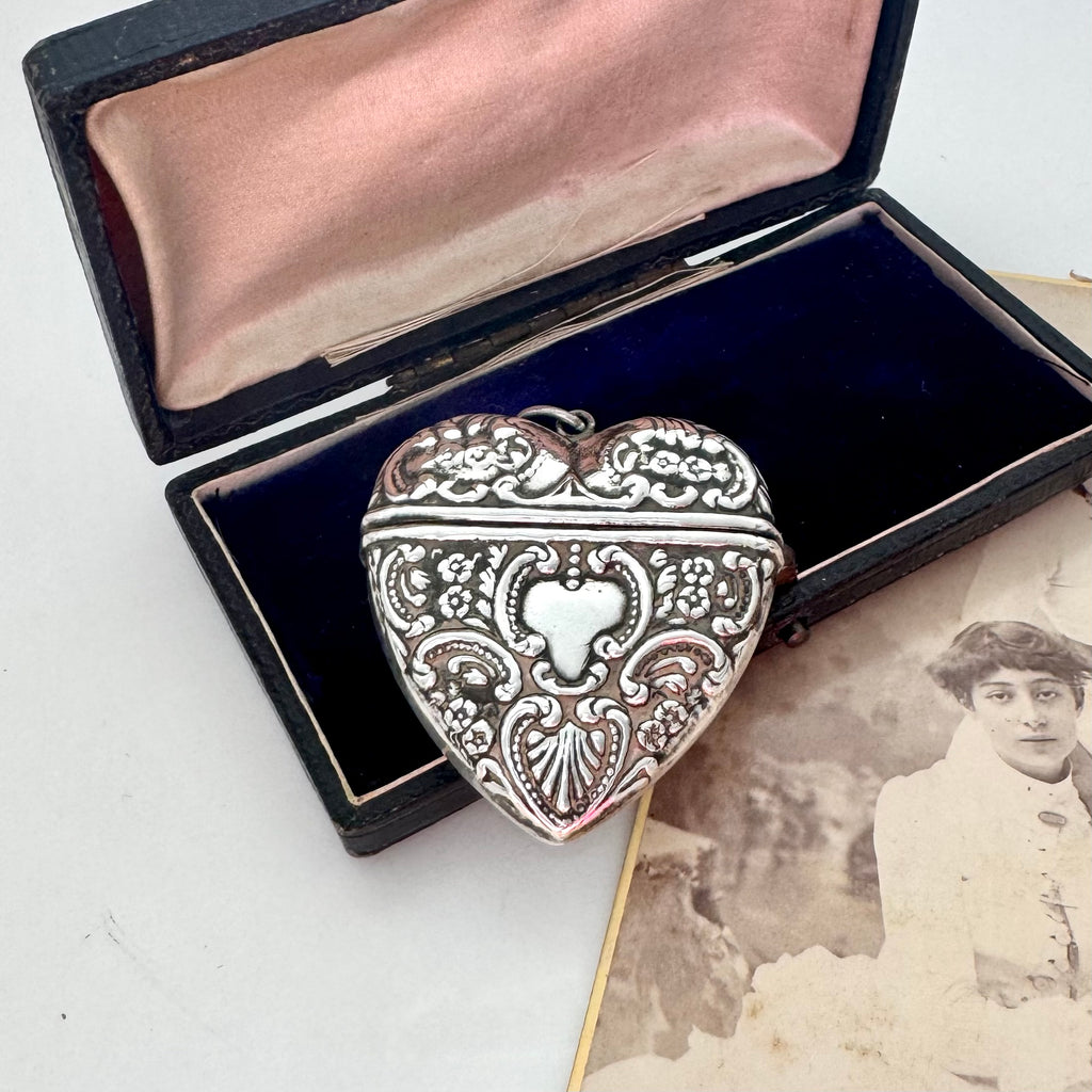 Decorative heart-shaped silver pendant in an open box with a vintage photograph underneath.