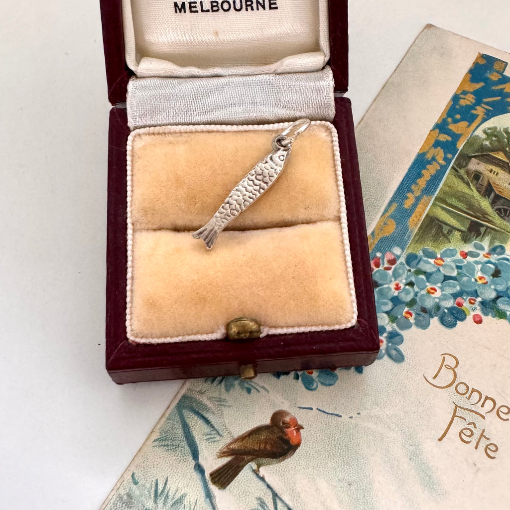 Silver fish charm in a jewelry box with vintage card in the background