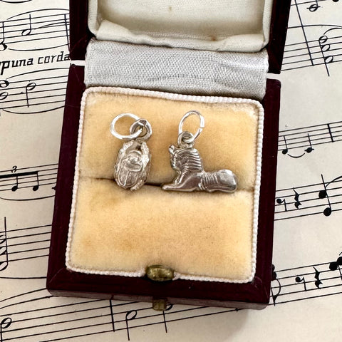 Silver vintage scarab beetle and sphinx charm in a jewelry box on sheet music