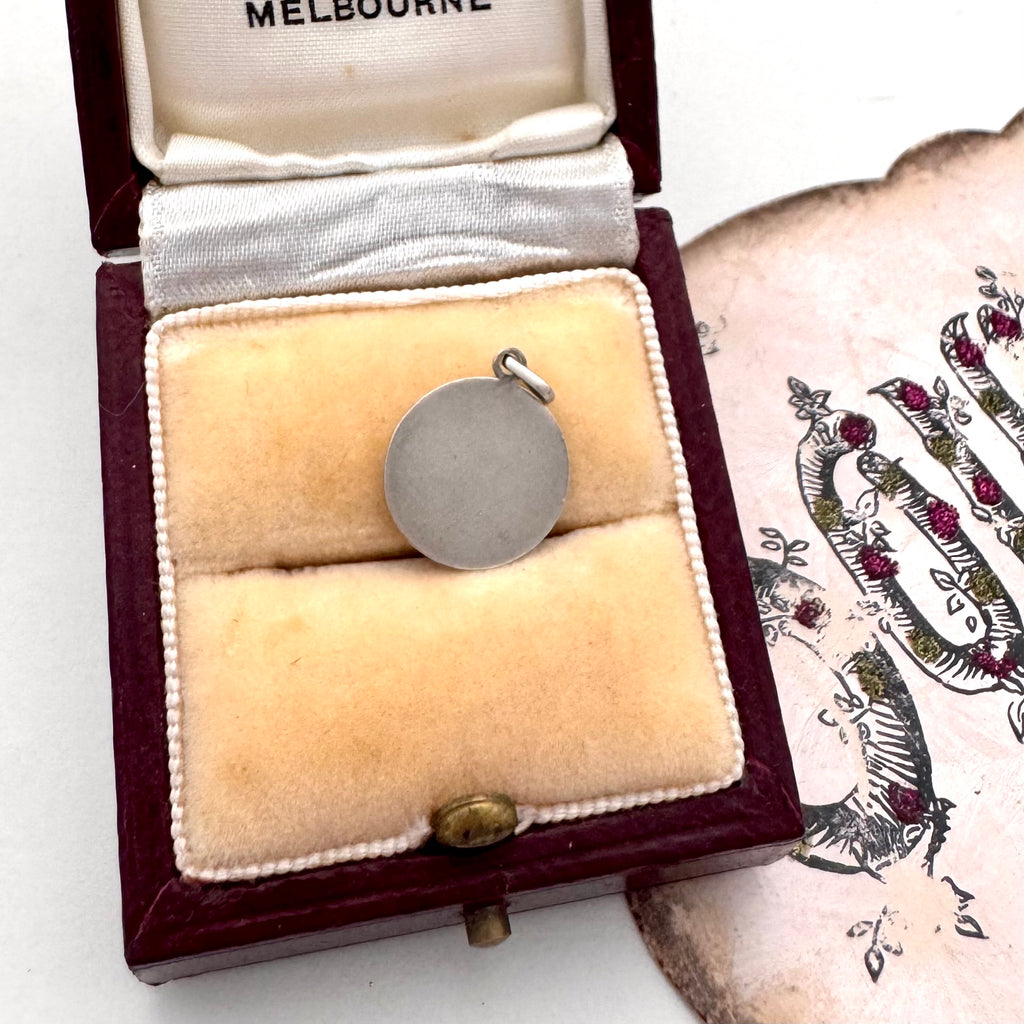 Silver pendant in a jewelry box with a decorative card in the background