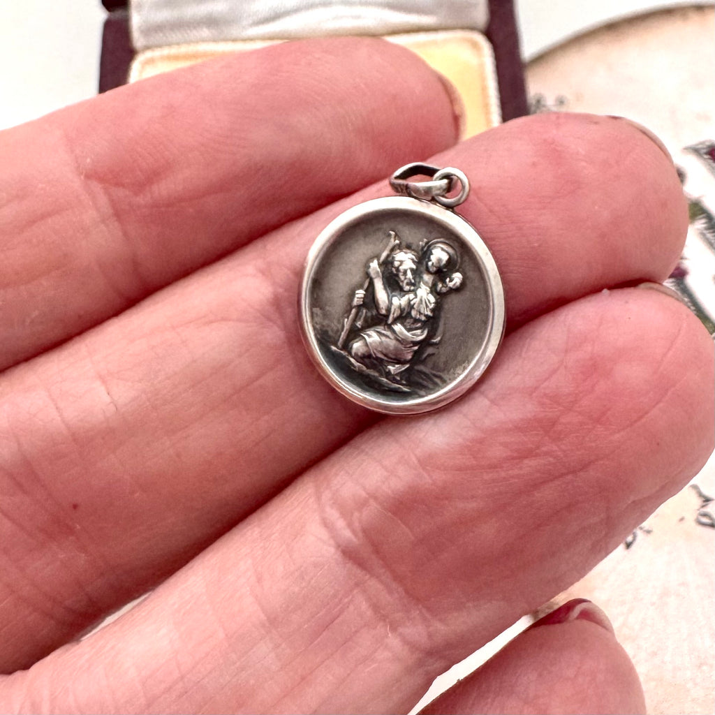 Silver vintage St Chrisopher charm held between fingers with a blurred background