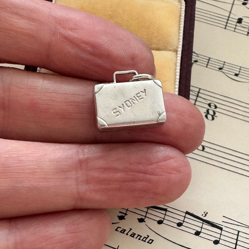 Silver suitcase charm on a finger with sheet music in the background