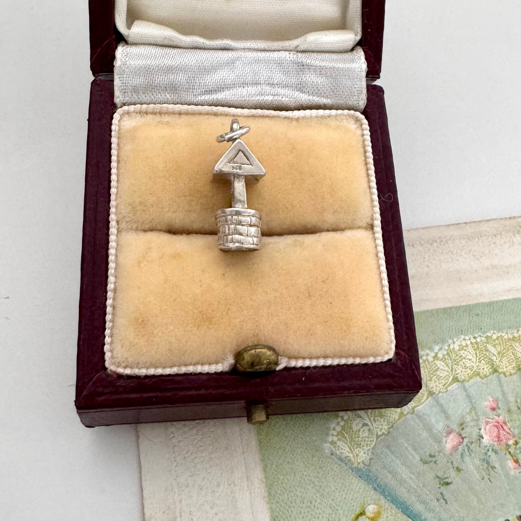 Vintage silver wishing well charm in an open jewelry box on a textured surface