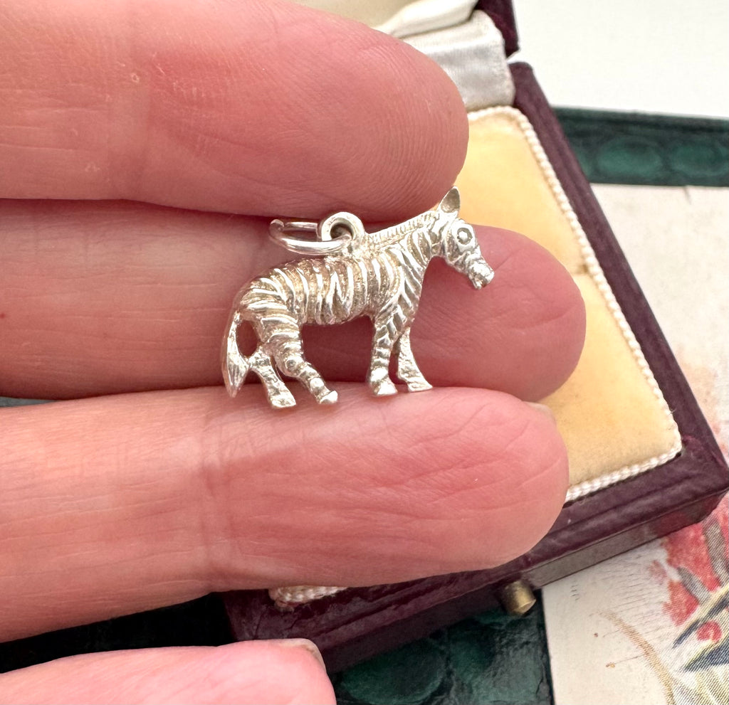 Silver zebra charm held between fingers with a jewelry box in the background