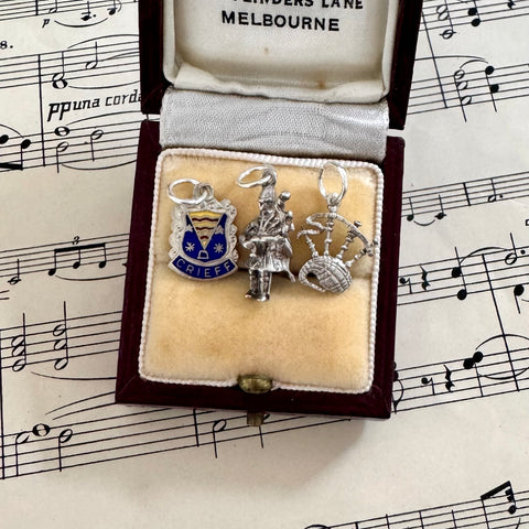Three vintage silver Scottish themed charms in a jewelry box on sheet music