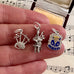 Three silver charms including a bagpipe, a person playing bagpipes, and a crest on a hand with sheet music in the background.