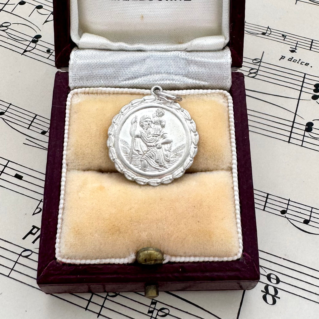 Silver St Christopher charm in a velvet-lined box on sheet music
