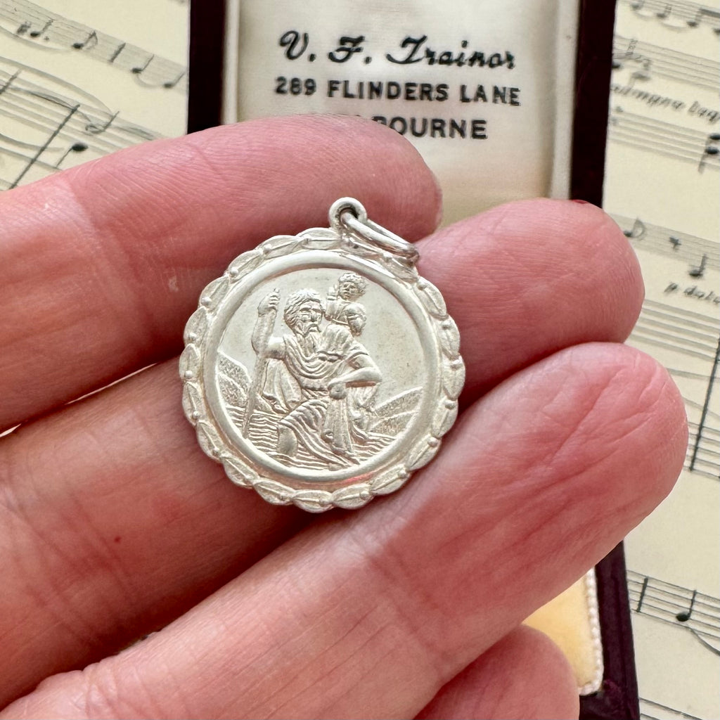 Silver St Christopher held between fingers with sheet music in the background
