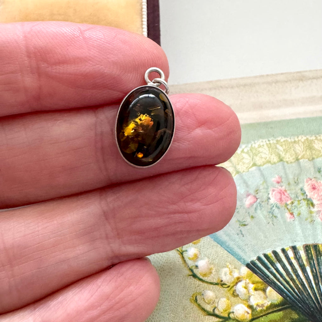 Silver pendant with an amber stone held between fingers against a floral background
