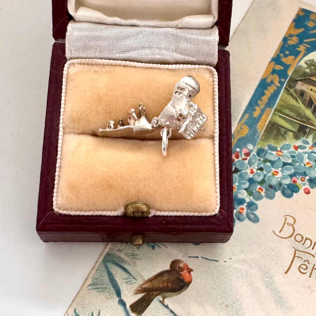 Vintage silver old woman in a shoe charm in a jewelry box on a decorative surface with floral patterns.