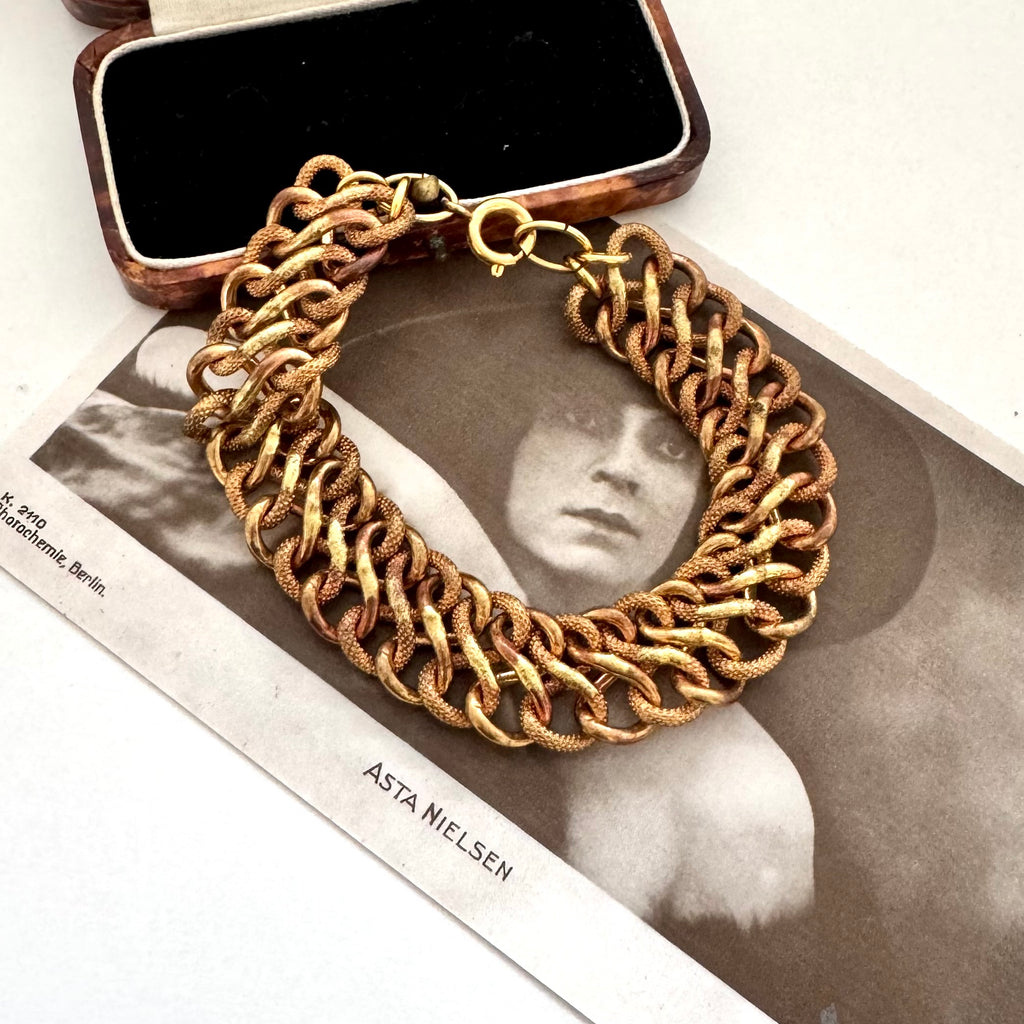 A vintage chunky gold-toned chain-link bracelet arranged on top of a vintage black-and-white photograph, with an open jewelry box partially visible behind it.