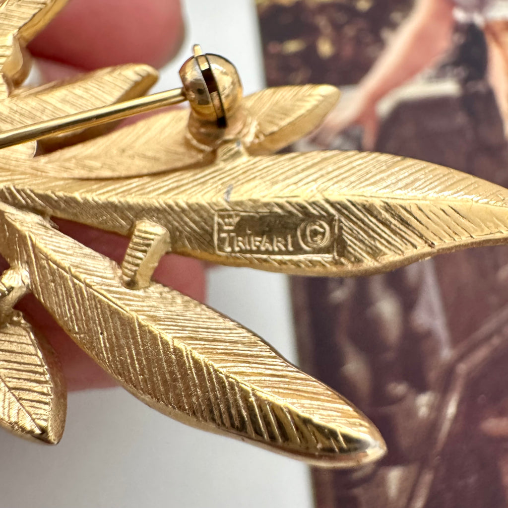 Gold feather-shaped brooch with 'Trifari' branding on a blurred background