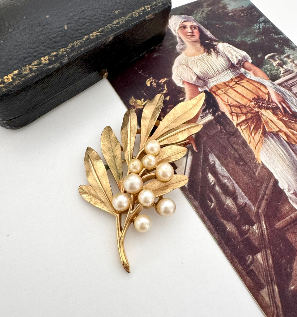 Trifari vintage gold leaf and pearl brooch with a black case and vintage illustration in the background
