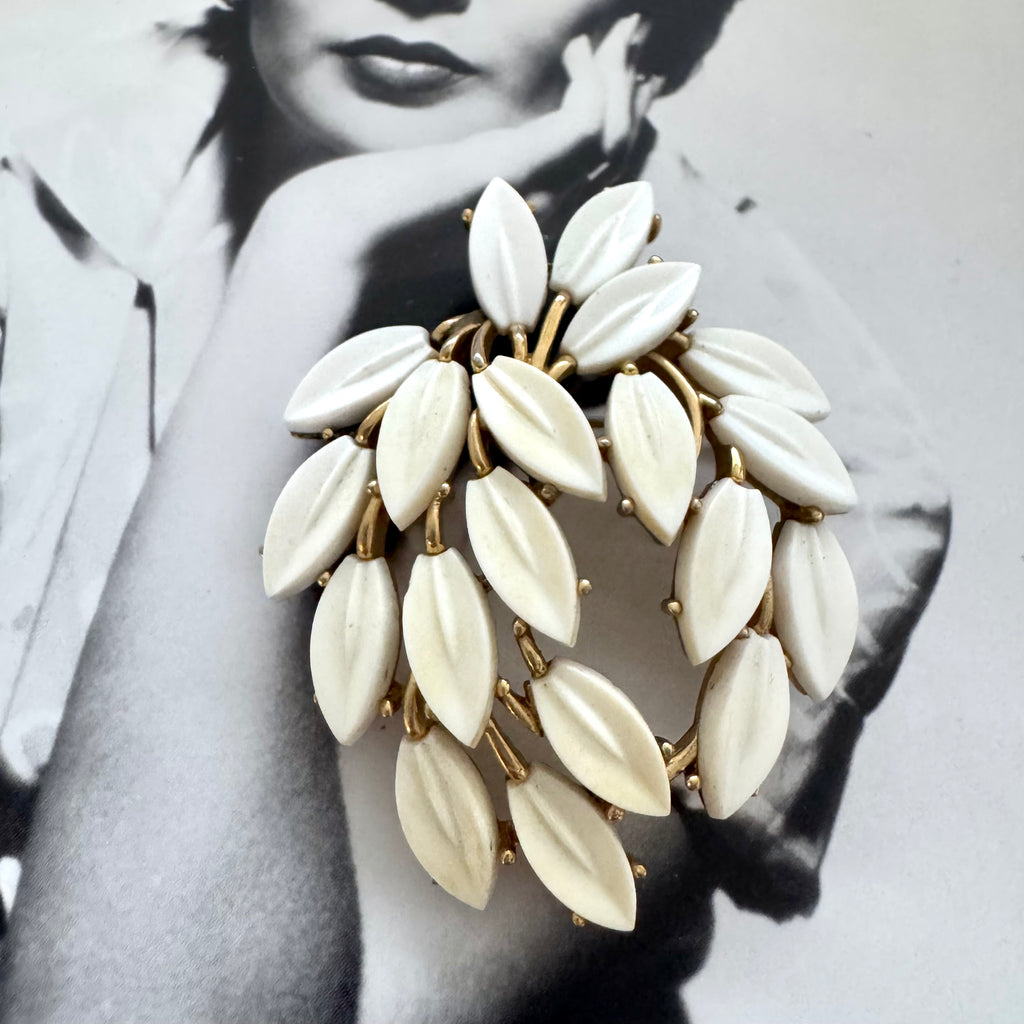 White vintage Trifari leaf-shaped brooch with gold accents on a black and white background
