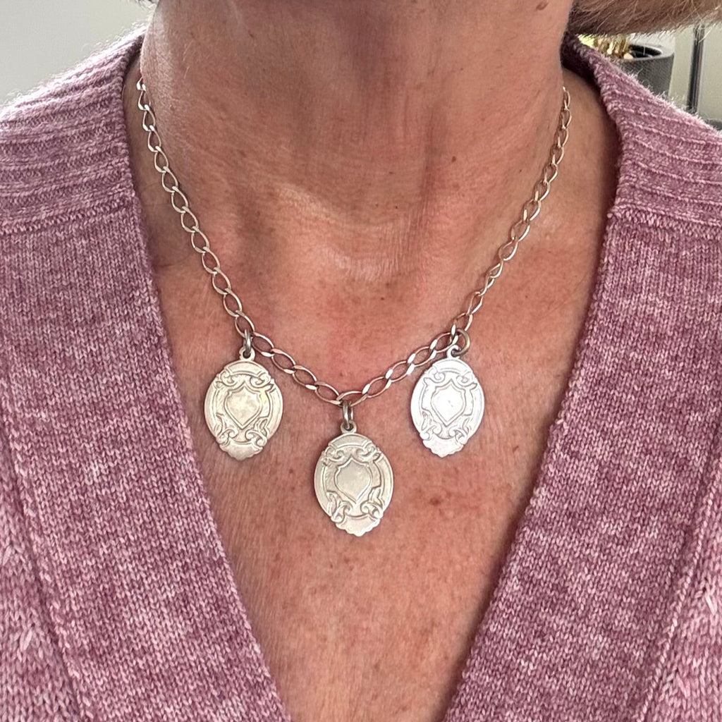 Close-up of a person wearing a silver necklace with three circular pendants on a pink garment.