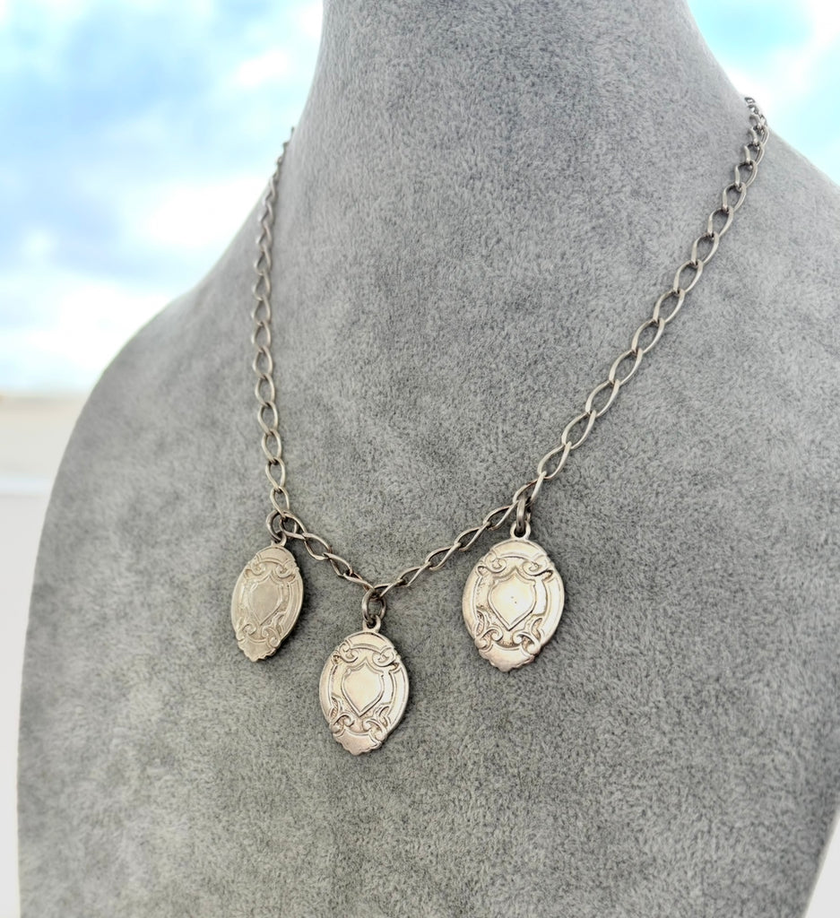 Silver necklace with pendant charms on a mannequin bust against a blurred outdoor background