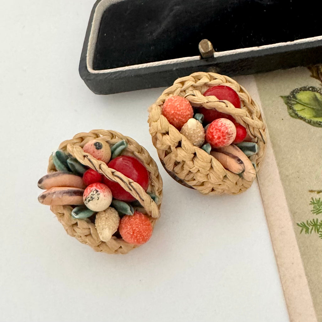 Pair of vintage earrings resembling woven baskets with fruit on a white surface.