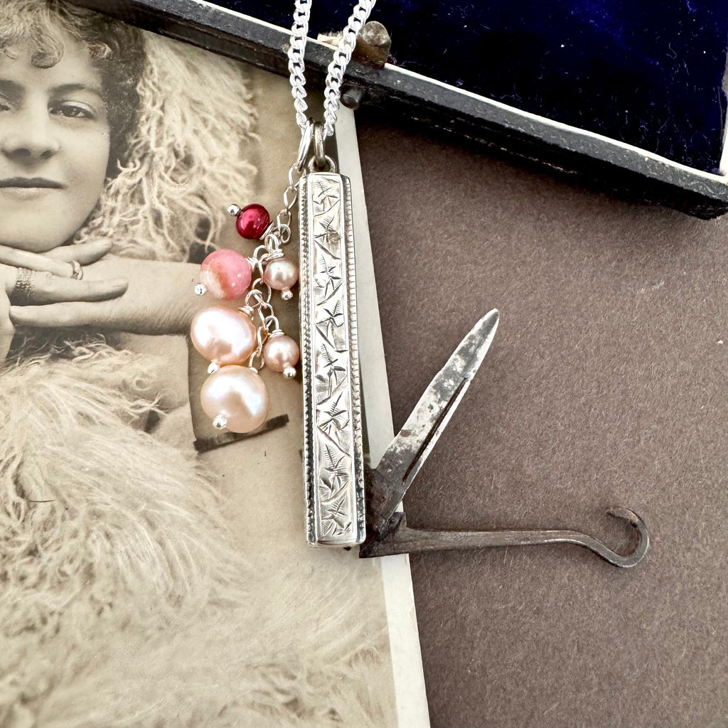 Vonk Jewellery antique 1885 button hook and pearl charm necklace on a brown background and with a vintage postcard and jewellery box