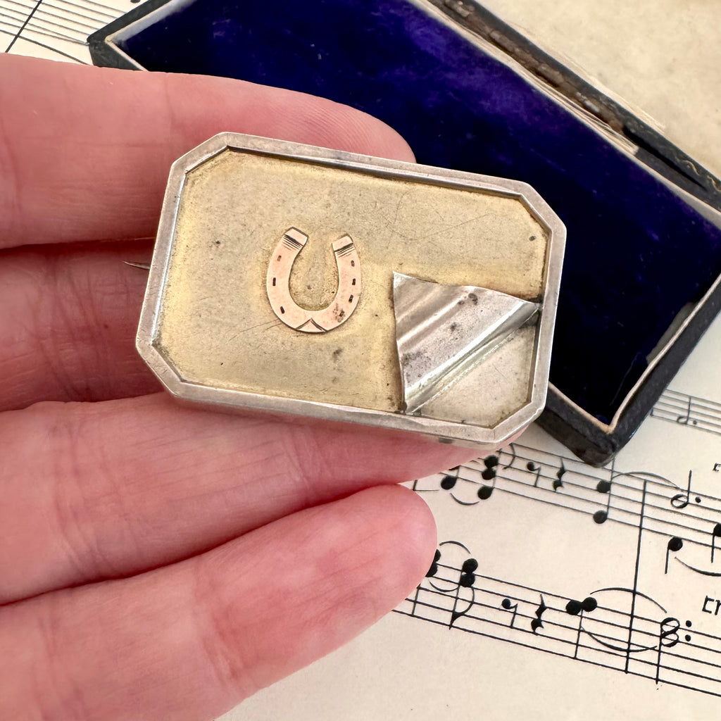 Vonk Jewellery antique silver horseshoe locket brooch on a vintage postcard, vintage sheet music and a vintage jewellery box. The brooch is in a woman's hand