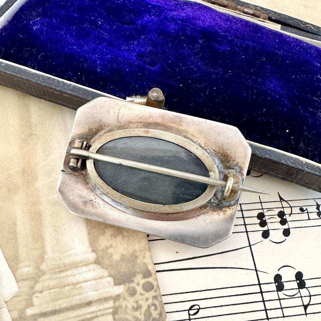 Back of Vonk Jewellery antique silver horseshoe locket brooch on a vintage postcard, vintage sheet music and a vintage jewellery box