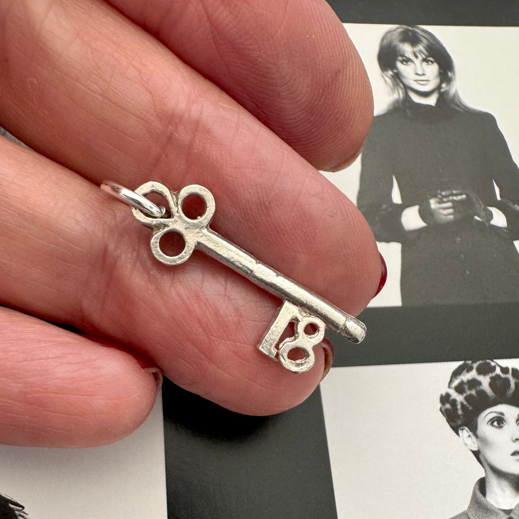 Vonk Jewellery vintage silver 18 Birthday key charm in a woman's hand and with a black and white image of models in the background.