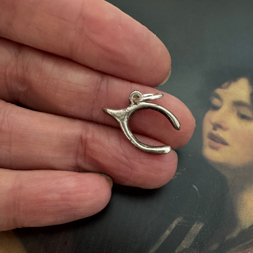 Vonk Jewellery silver vintage lucky wishbone charm on a picture of a woman playing a harp and in a woman's hand