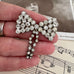 Vonk Jewellery vintage 1950's rhinestone bow brooch on a vintage postcard and vintage sheet music and in a woman's hand