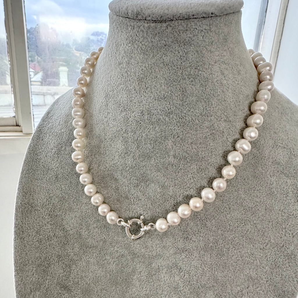Pearl necklace on a mannequin bust with a blurred outdoor background
