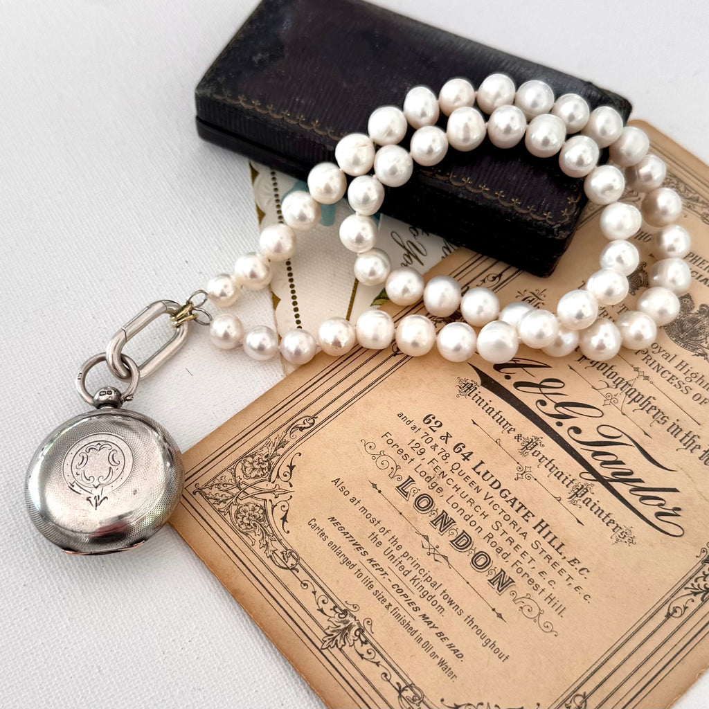 Pearl necklace with a silver pocket watch on an old document