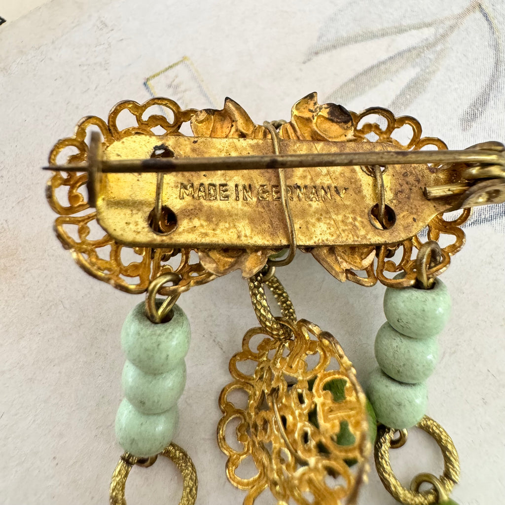 Back of Vonk jewellery Made In Germany vintage gold tone and green bead dangle brooch on a vintage postcard