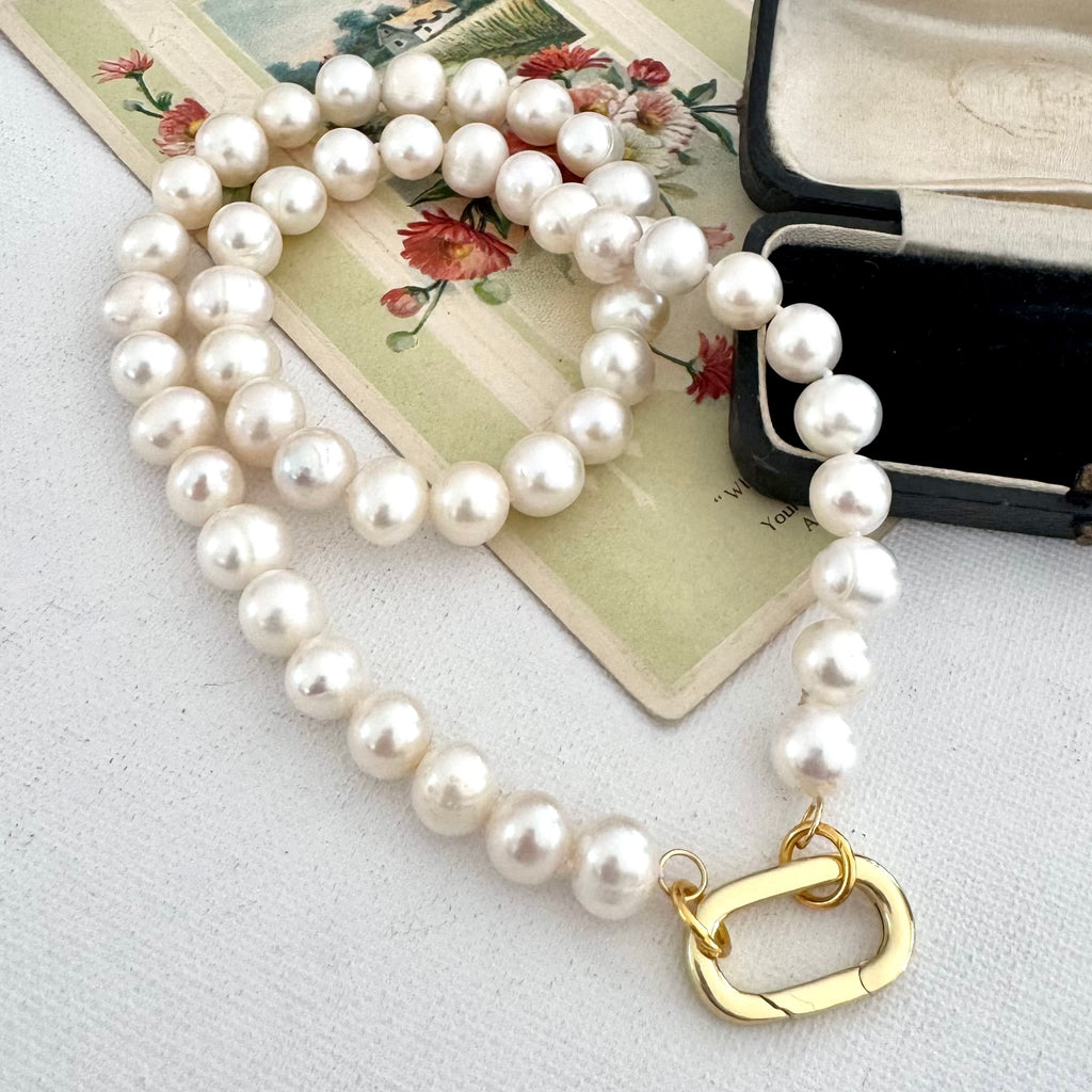 A strand of white freshwater pearls with a gold clasp, arranged on a vintage floral card next to an open black jewelry box.