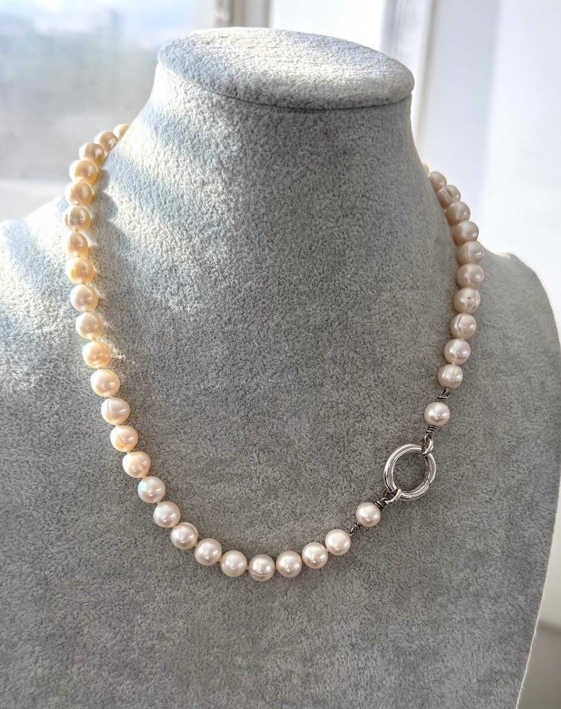 Pearl necklace on a gray mannequin bust with a blurred window background