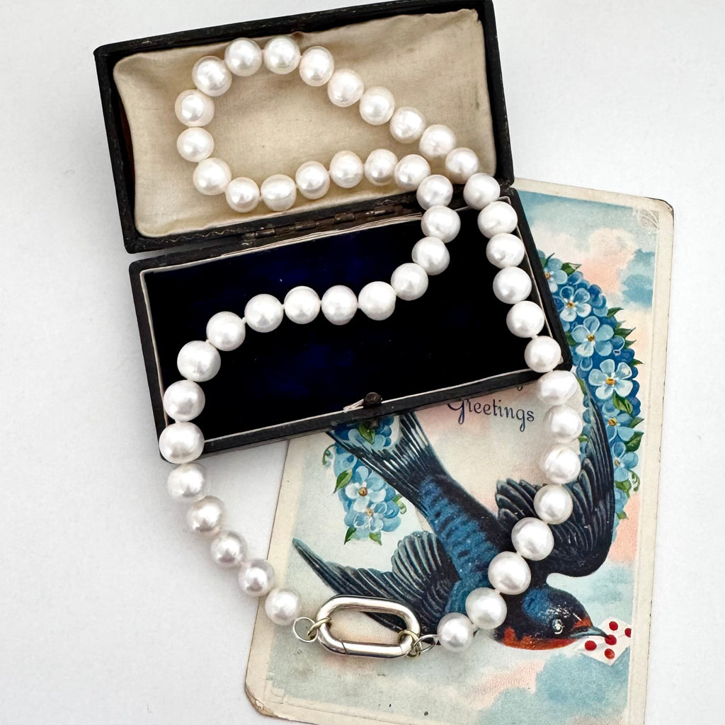 Pearl necklace in an open jewelry box with a vintage card featuring a bird and flowers.