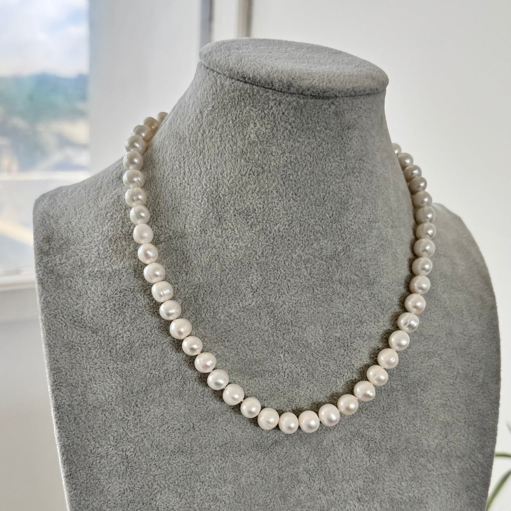 Pearl necklace on a gray mannequin bust with a blurred outdoor background