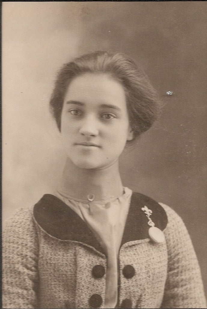A vintage sepia-toned portrait photograph of a young woman wearing a textured tweed jacket with a dark collar and a decorative brooch.