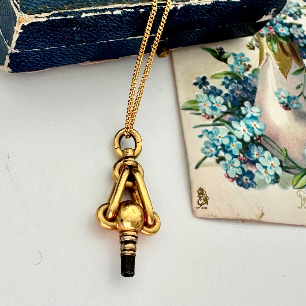 Gold necklace with an antique pocket watch key on a white surface with floral card in the background
