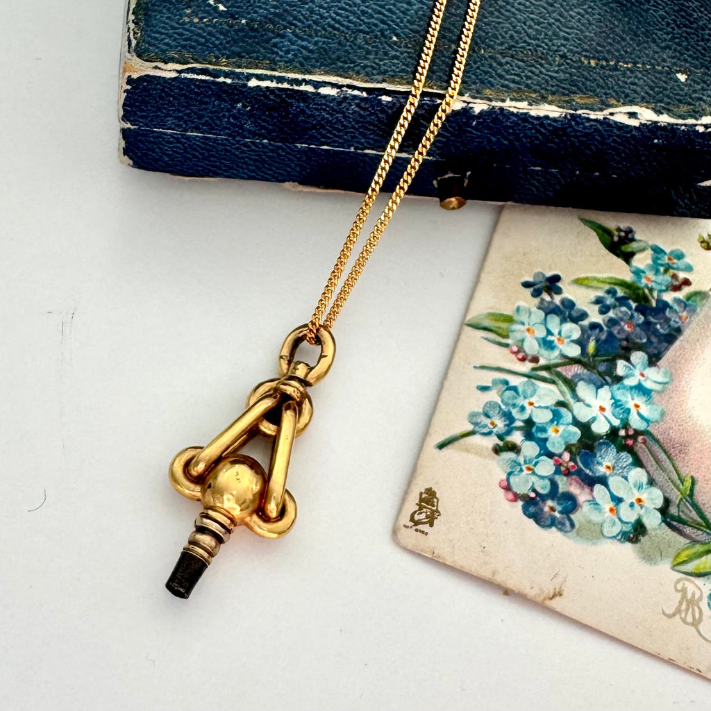 Gold necklace with an antique pocket watch key on a white surface with floral card in the background