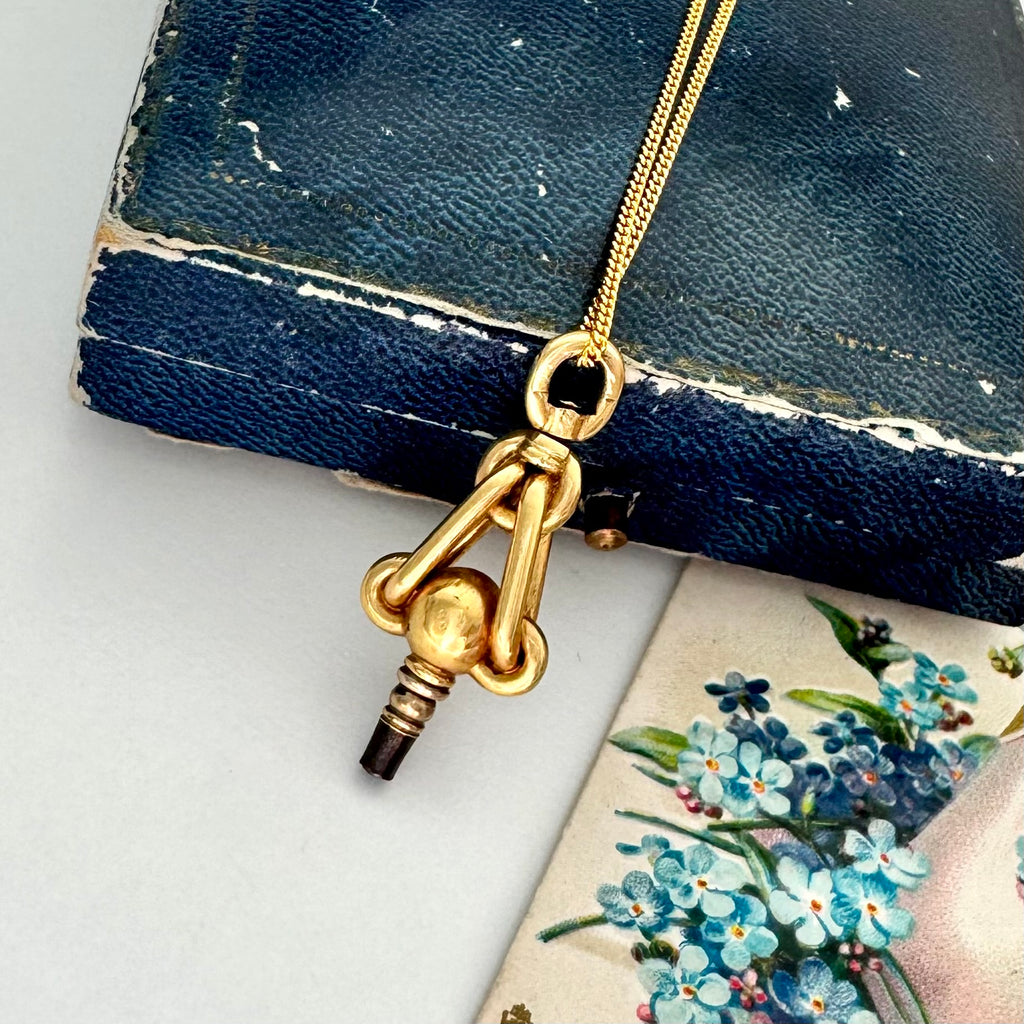 Gold necklace with an antique pocket watch key on a white surface with floral card in the background