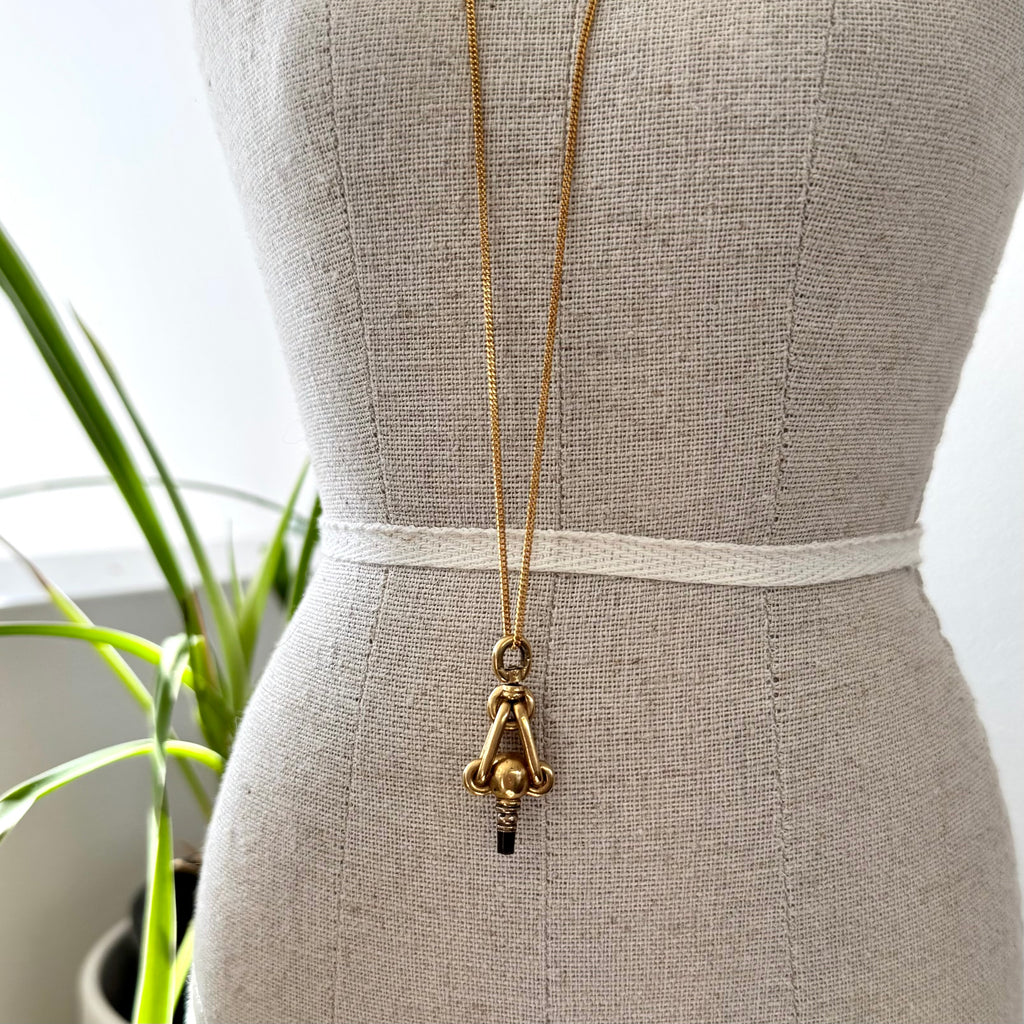 Gold necklace with an antique pocket watch key on a mannequin against a neutral background