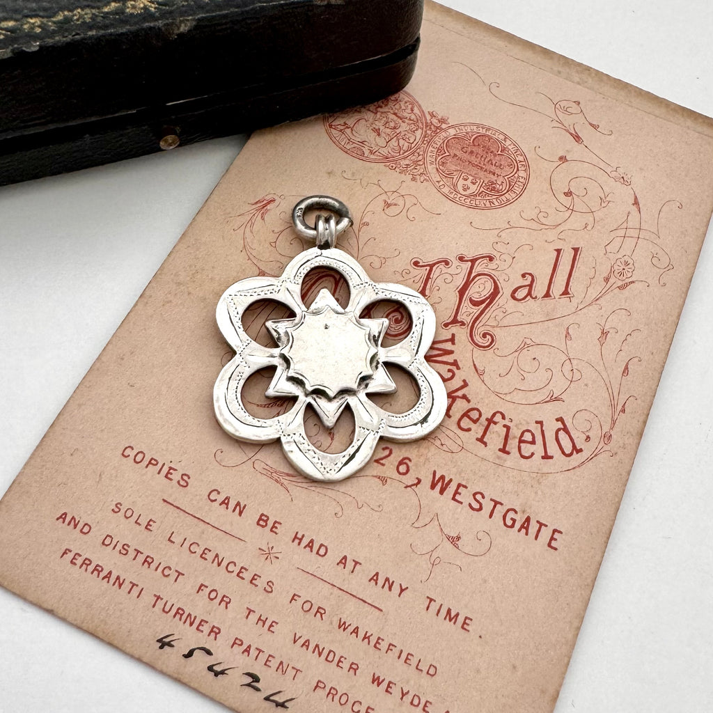 Silver floral antique watch fob pendant on an old document with a vintage feel