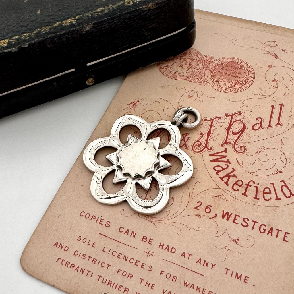 Silver floral antique watch fob pendant on an old document with a vintage feel