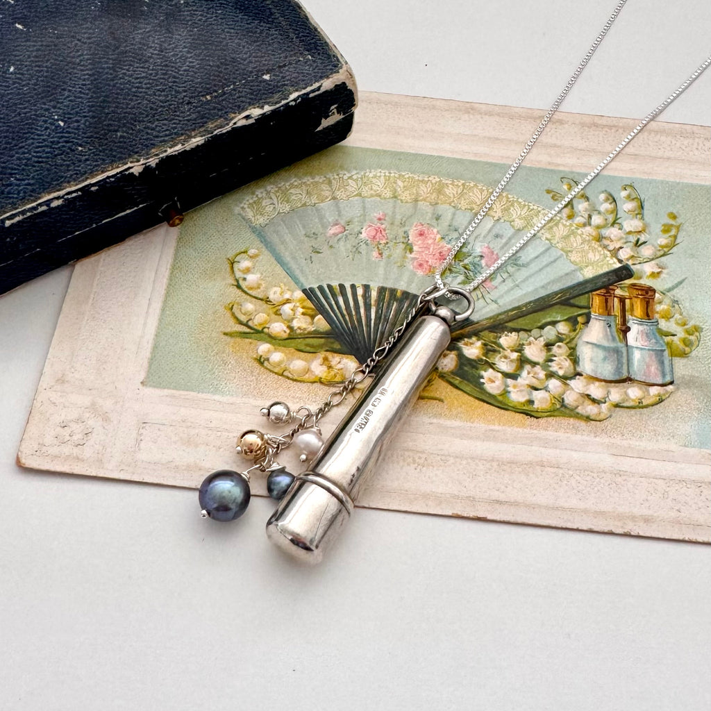 Antique silver cheroot holder and pearl charm necklace on a vintage-style card with floral design