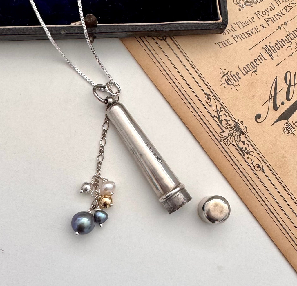 Antique silver cheroot holder and pearl charm necklace on a vintage-style card with floral design