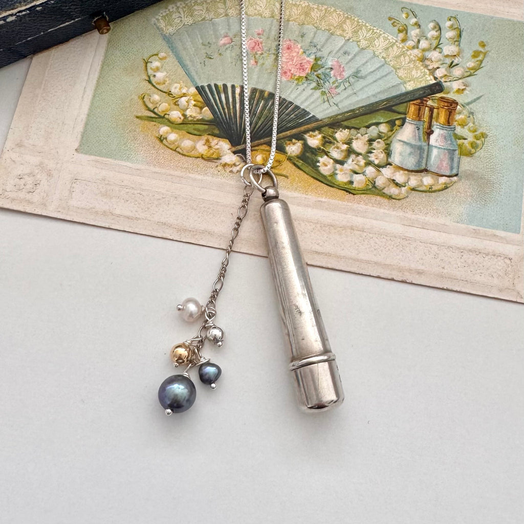 Antique silver cheroot holder and pearl charm necklace on a vintage-style card with floral design