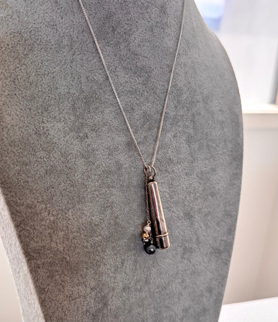 Antique silver cheroot holder and pearl charm necklace on a grey mannequin